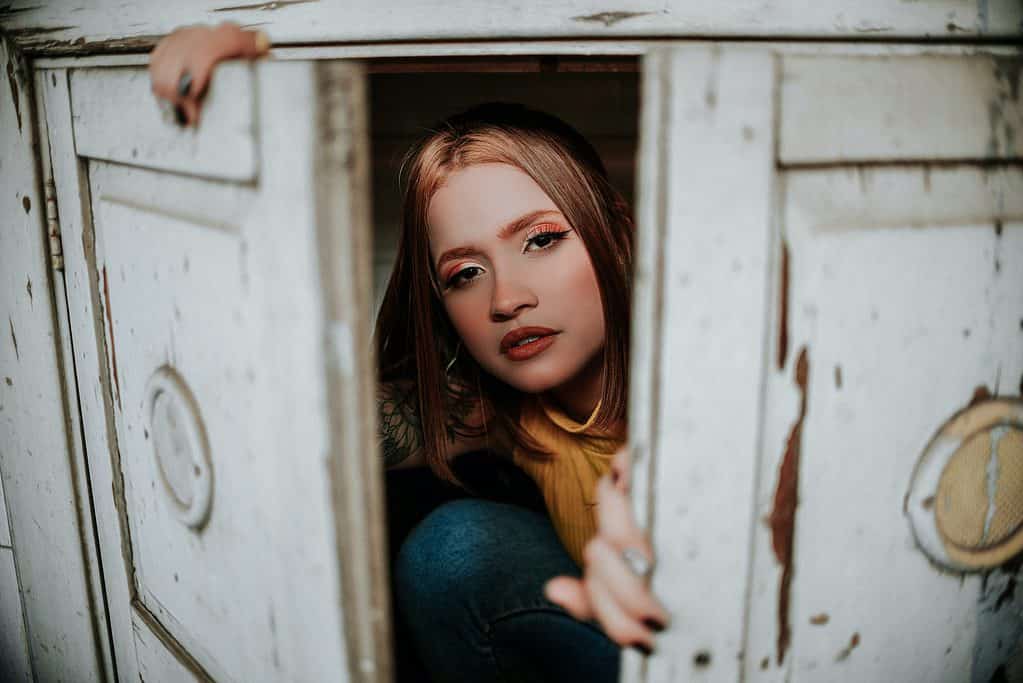 a woman in blue denim jeans hiding inside white wooden cabinet